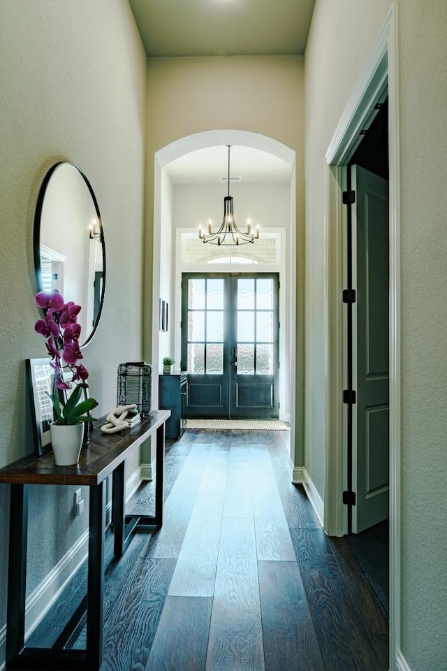 interior space with baseboards, french doors, arched walkways, a notable chandelier, and dark wood-style flooring