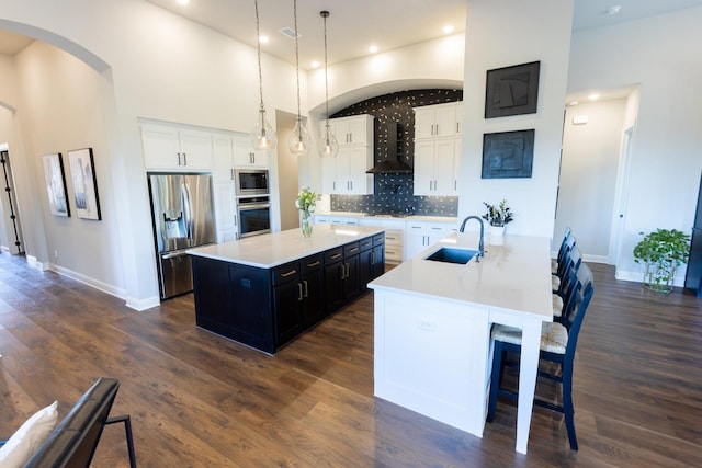 kitchen featuring a sink, a spacious island, appliances with stainless steel finishes, wall chimney exhaust hood, and light countertops