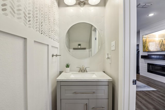 bathroom with a glass covered fireplace, visible vents, vanity, and wood finished floors