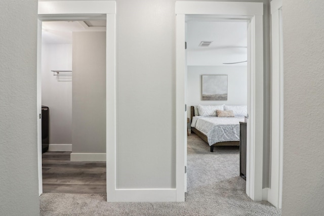 hallway featuring carpet, visible vents, a textured wall, wood finished floors, and baseboards