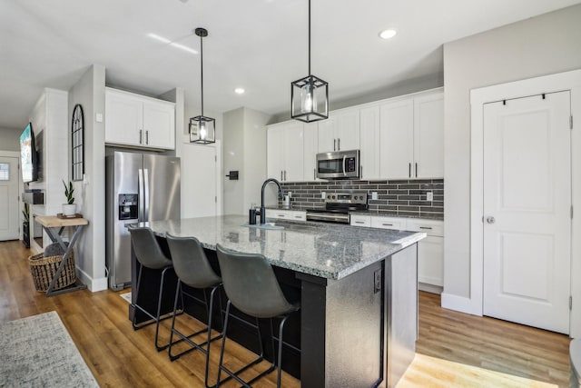 kitchen with stainless steel appliances, backsplash, light wood-style flooring, an island with sink, and light stone countertops