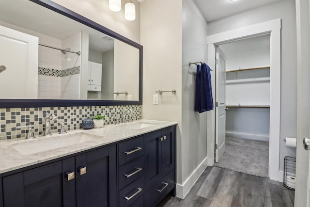 bathroom featuring a walk in closet, a sink, decorative backsplash, and wood finished floors