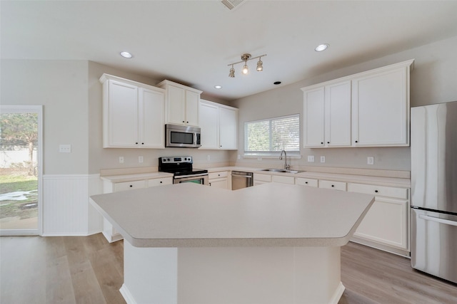 kitchen with stainless steel appliances, light wood-type flooring, a sink, and a kitchen island