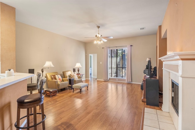 living area with ceiling fan, light wood-style flooring, a fireplace, visible vents, and baseboards