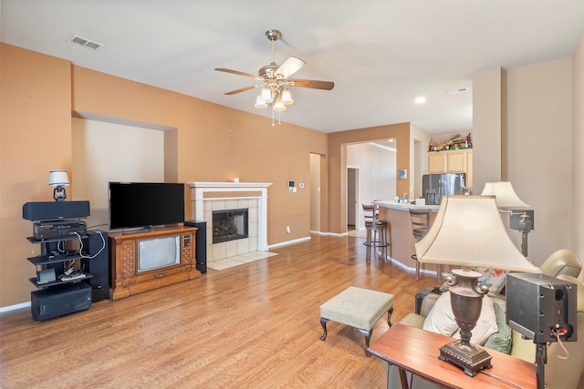 living area with light wood finished floors, a tiled fireplace, visible vents, and baseboards