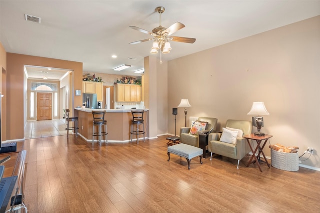 living room featuring light wood finished floors, a ceiling fan, visible vents, and baseboards