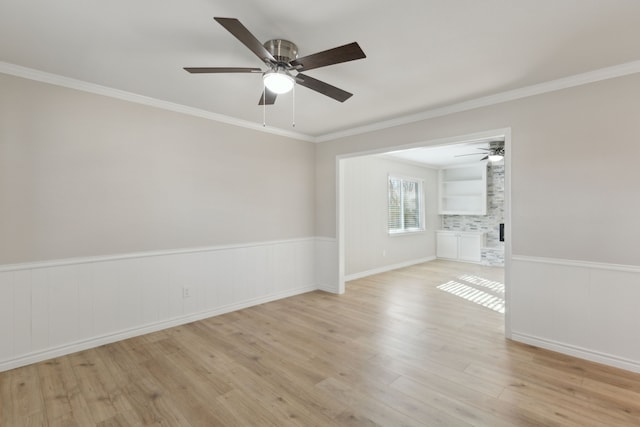 spare room with a wainscoted wall, light wood-style flooring, and crown molding