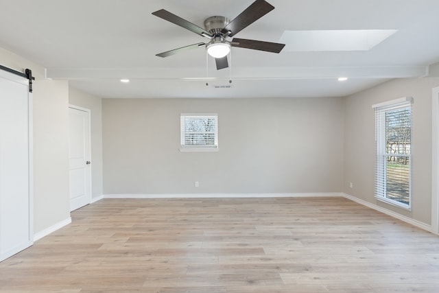 empty room featuring light wood-style flooring, baseboards, and a barn door