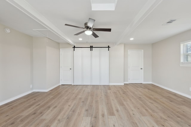 unfurnished bedroom featuring light wood finished floors, visible vents, a barn door, attic access, and baseboards