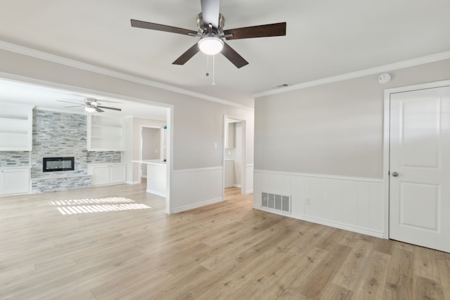 unfurnished living room with a wainscoted wall, a fireplace, visible vents, and light wood finished floors