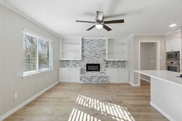 unfurnished living room with a fireplace, a ceiling fan, baseboards, light wood-type flooring, and crown molding