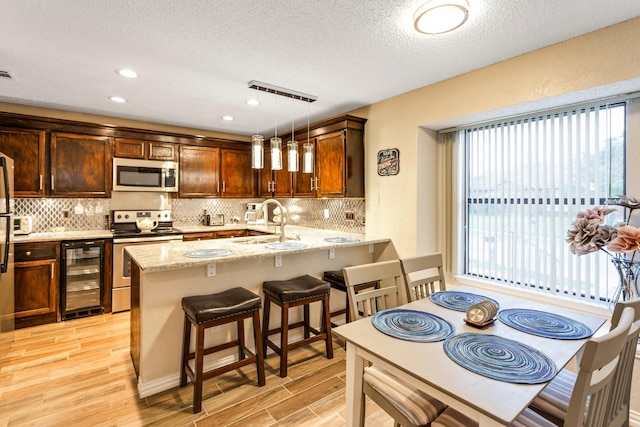 kitchen with wine cooler, light wood finished floors, appliances with stainless steel finishes, a sink, and a peninsula