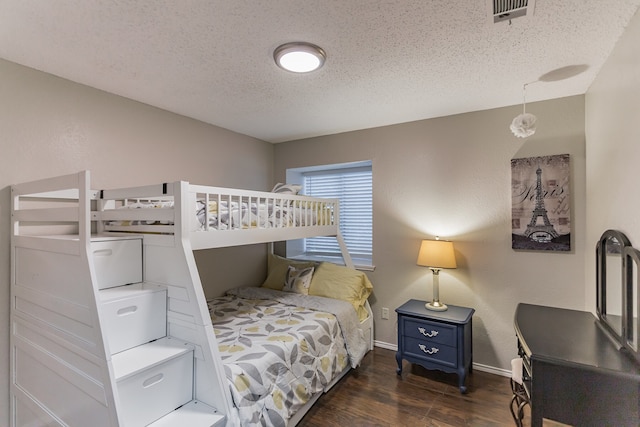 bedroom featuring visible vents, a textured ceiling, baseboards, and wood finished floors