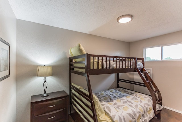 bedroom featuring baseboards, wood finished floors, a textured ceiling, and a textured wall