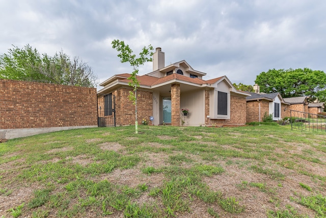 view of front facade with brick siding, fence, a chimney, and a front lawn