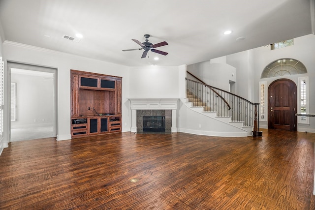 unfurnished living room with visible vents, a tile fireplace, ceiling fan, wood finished floors, and stairs