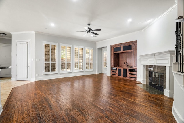 unfurnished living room with baseboards, ceiling fan, wood finished floors, crown molding, and a fireplace