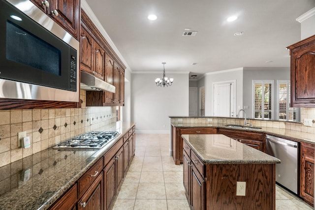 kitchen with light tile patterned flooring, under cabinet range hood, a sink, ornamental molding, and appliances with stainless steel finishes