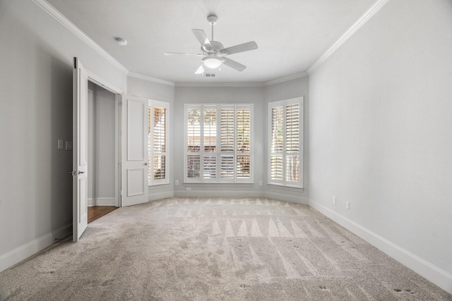 carpeted spare room featuring baseboards, visible vents, ceiling fan, and crown molding