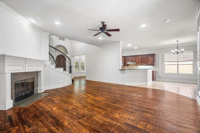 unfurnished living room with crown molding, a fireplace, baseboards, and ceiling fan with notable chandelier