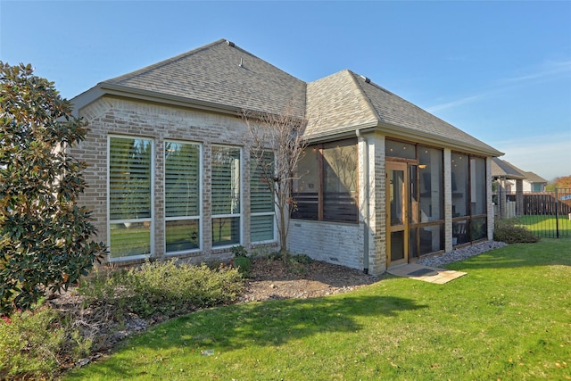 rear view of property with a sunroom, brick siding, a yard, and roof with shingles