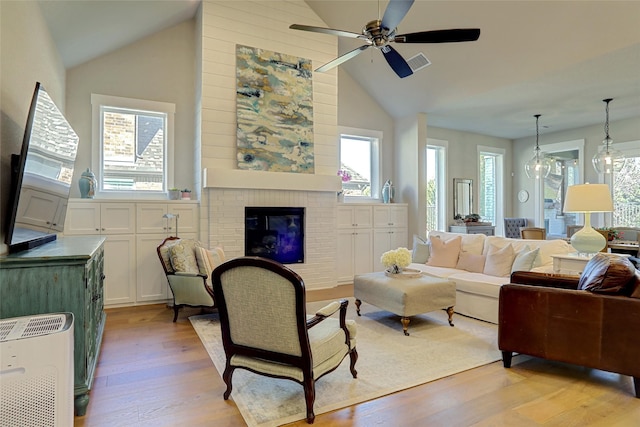 living area with a brick fireplace, visible vents, ceiling fan, light wood-style floors, and high vaulted ceiling