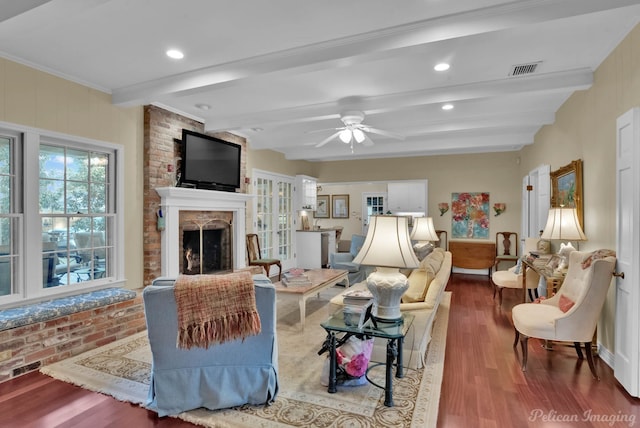 living area featuring a large fireplace, visible vents, ceiling fan, wood finished floors, and beam ceiling