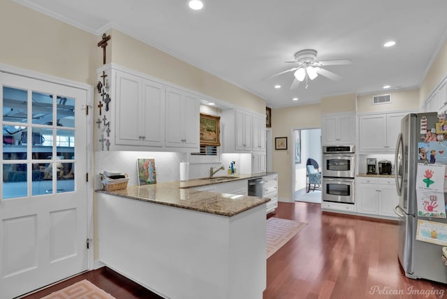 kitchen with visible vents, appliances with stainless steel finishes, light stone counters, a peninsula, and backsplash