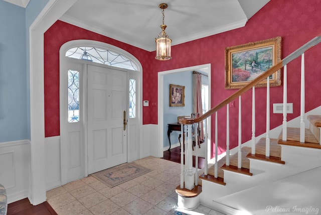 foyer with a wainscoted wall, crown molding, wallpapered walls, and stairs