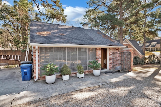 back of property with brick siding, roof with shingles, and fence