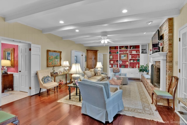 living room featuring built in shelves, beamed ceiling, a brick fireplace, and wood finished floors