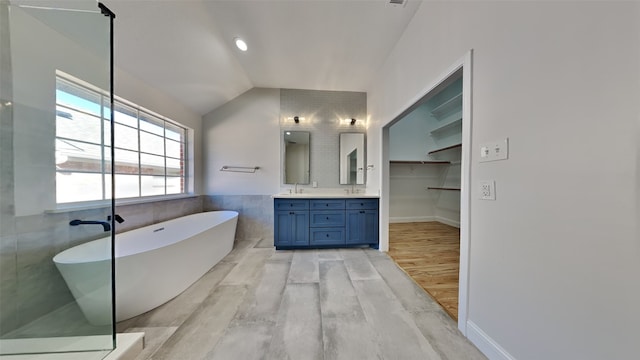 full bathroom featuring lofted ceiling, wood finished floors, a sink, a freestanding bath, and double vanity