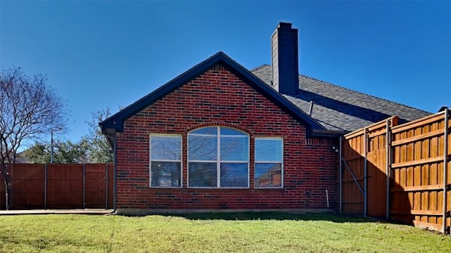 view of side of home with brick siding, a chimney, a shingled roof, a lawn, and fence