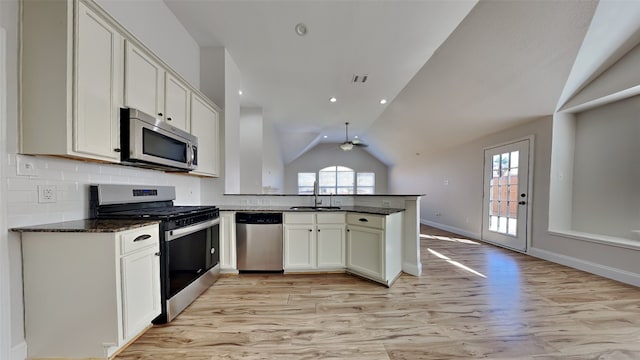 kitchen featuring a peninsula, a sink, vaulted ceiling, appliances with stainless steel finishes, and tasteful backsplash