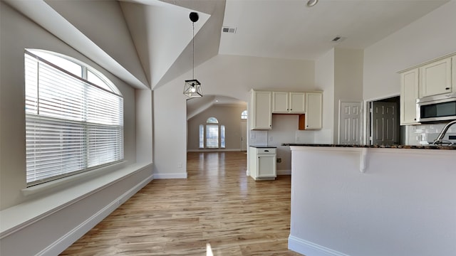 kitchen featuring light wood-style flooring, stainless steel microwave, backsplash, and visible vents