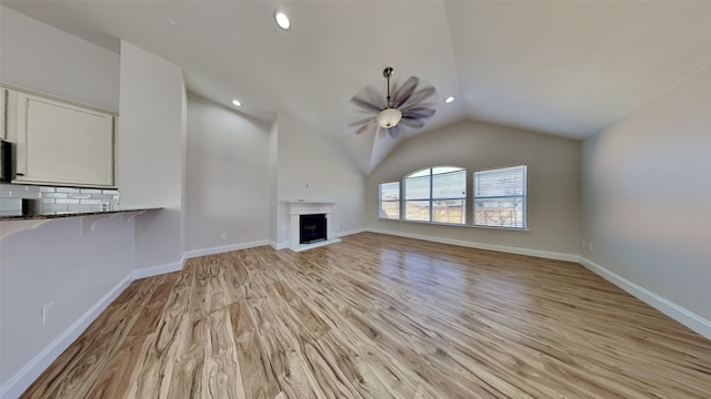 unfurnished living room with a fireplace with raised hearth, lofted ceiling, a ceiling fan, baseboards, and light wood-type flooring