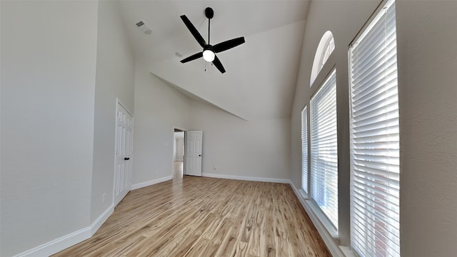 unfurnished living room with baseboards, visible vents, light wood-style flooring, ceiling fan, and a high ceiling