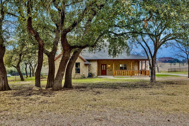 view of front of home with a porch, stone siding, fence, and a front lawn