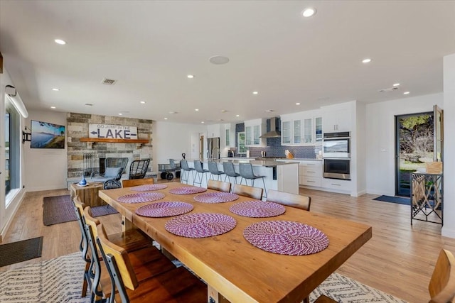 dining space with light wood finished floors, a stone fireplace, and recessed lighting