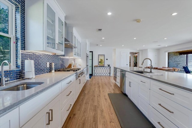 kitchen with appliances with stainless steel finishes, backsplash, a sink, and light wood-style flooring