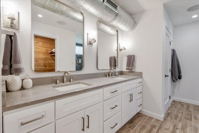 bathroom featuring baseboards, double vanity, a sink, and wood tiled floor