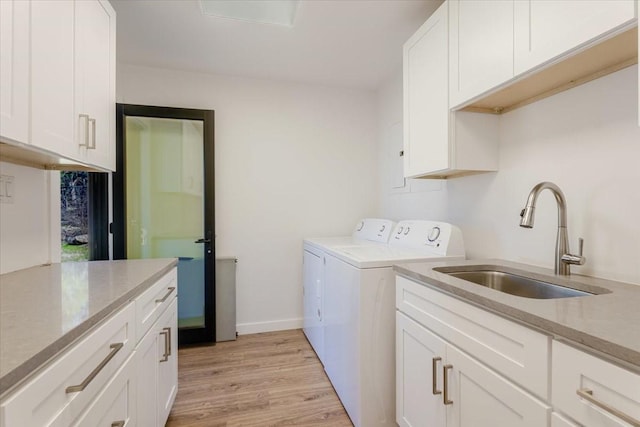 washroom featuring cabinet space, baseboards, washing machine and clothes dryer, light wood-type flooring, and a sink