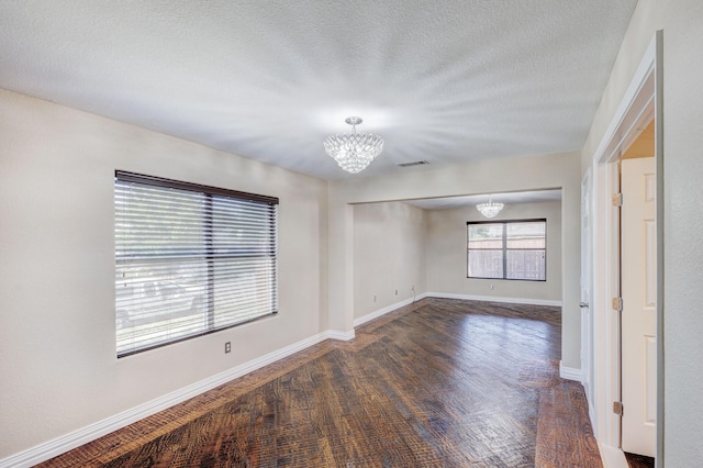 spare room with a chandelier, visible vents, a textured ceiling, and baseboards