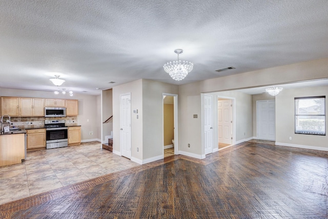 kitchen with appliances with stainless steel finishes, open floor plan, a sink, light brown cabinets, and a notable chandelier