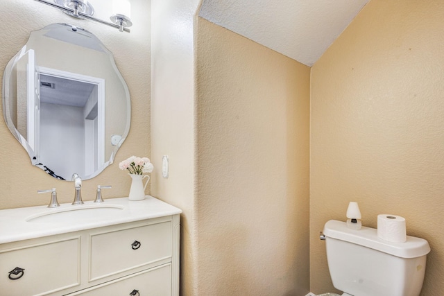 bathroom featuring toilet, a textured wall, and vanity