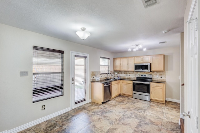 kitchen with appliances with stainless steel finishes, dark countertops, visible vents, and light brown cabinetry