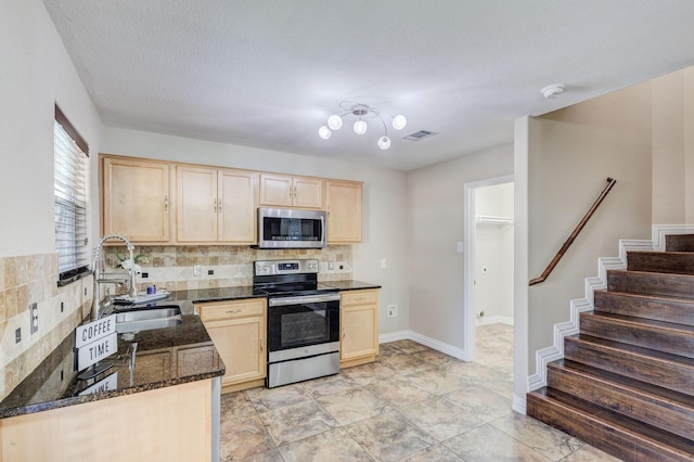 kitchen featuring tasteful backsplash, appliances with stainless steel finishes, dark stone countertops, light brown cabinetry, and a sink