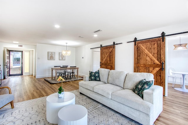 living area with a barn door, light wood-style flooring, visible vents, and baseboards