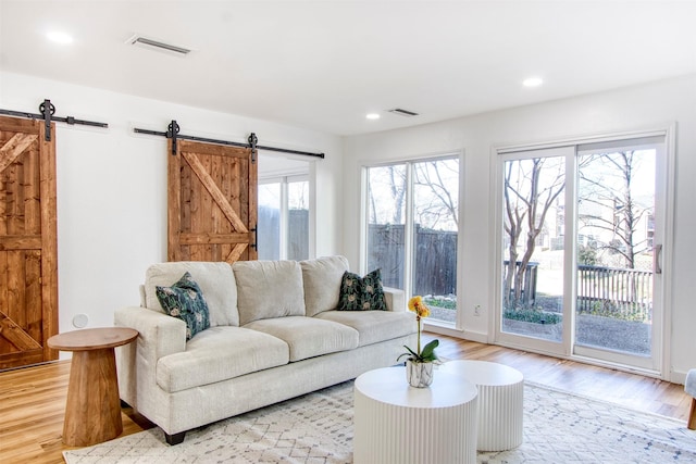 living area featuring recessed lighting, visible vents, light wood-style flooring, and a barn door