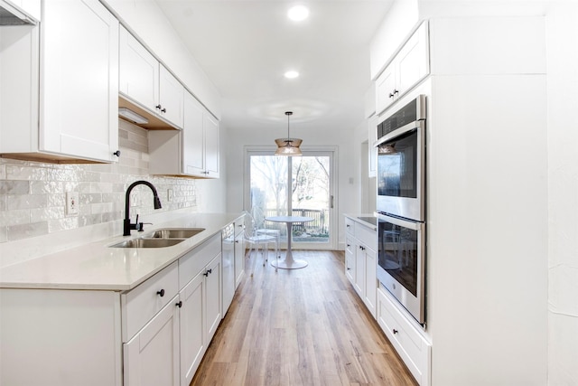 kitchen featuring tasteful backsplash, light wood-style flooring, light countertops, double oven, and a sink